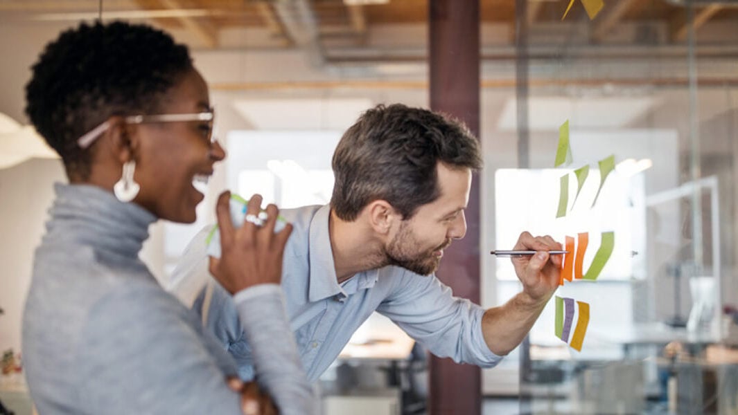 Male and female colleagues working collaboratively at a glass whiteboard